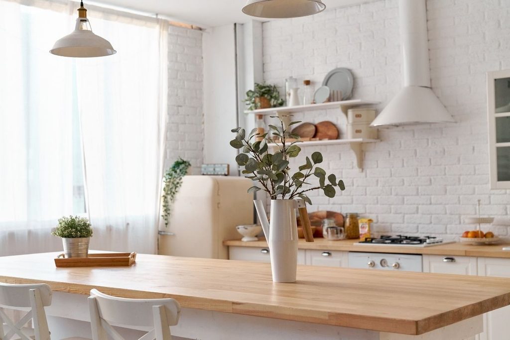 A kitchen with a butcher-block island, white brick wall and open shelving styled with eucalyptus