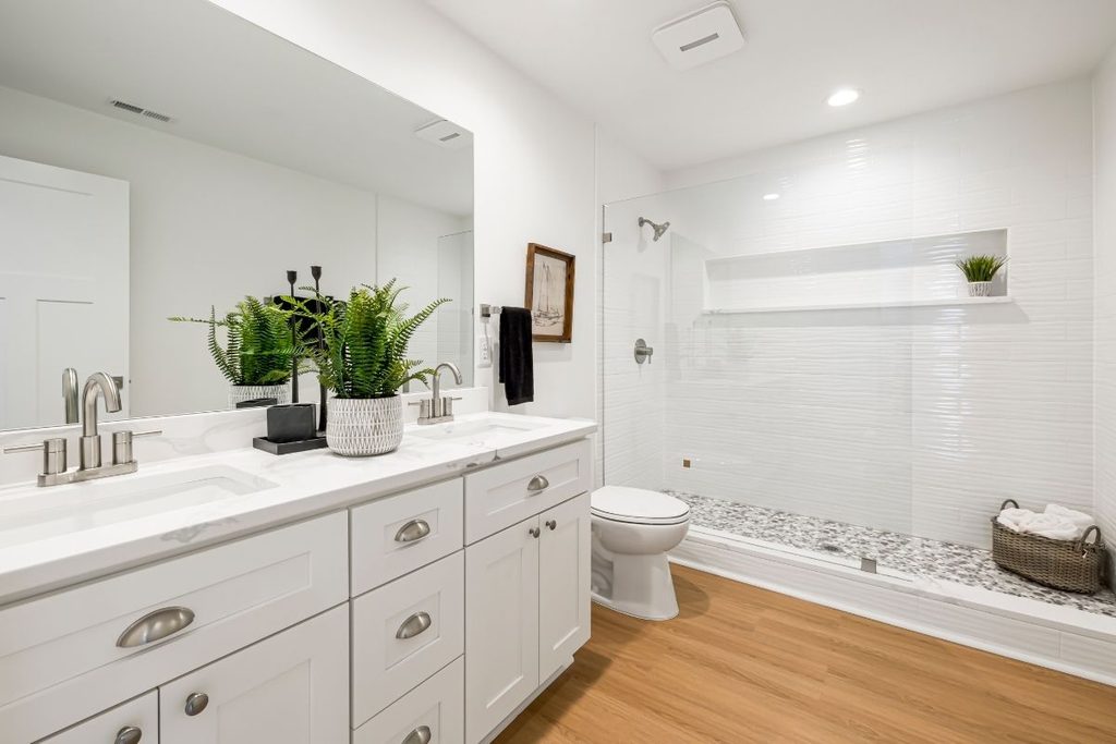 A clean white bathroom with a double vanity, glass shower and wood-look flooring
