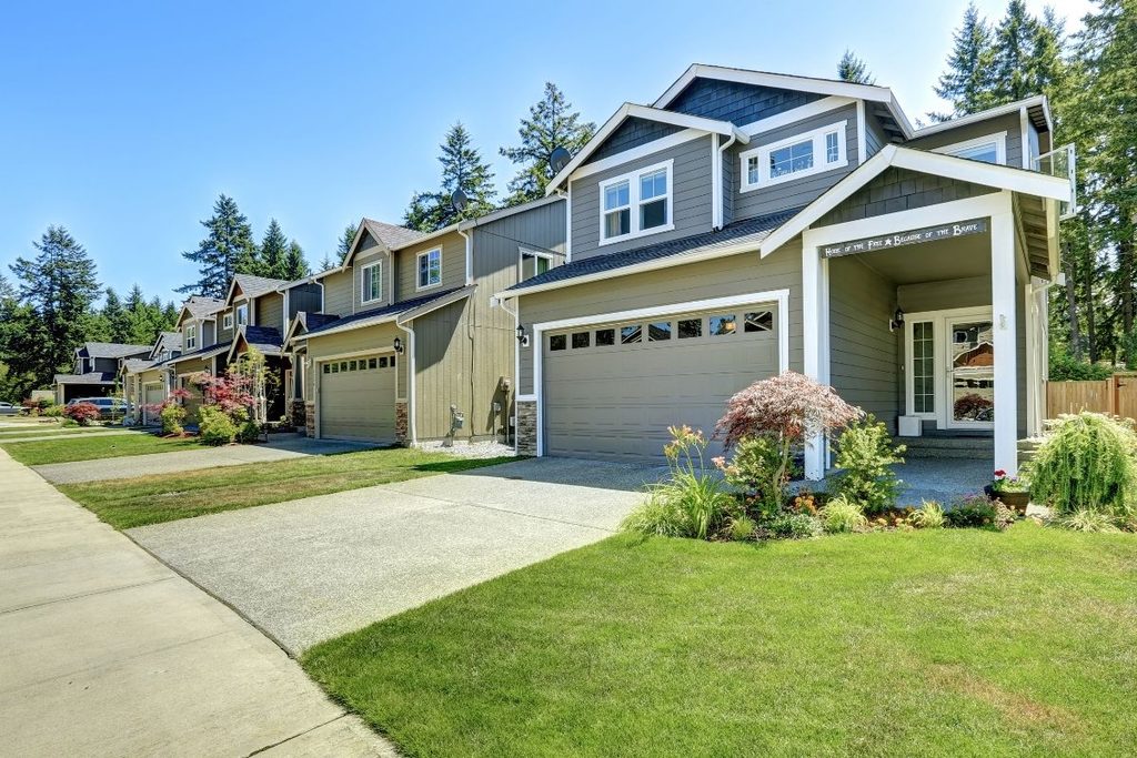 The exterior of a gray two-story home with a two-car garage, a landscaped yard and tall evergreen trees