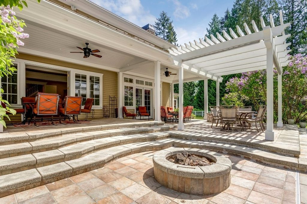 A covered patio with a white pergola, outdoor seating and a stone fire pit