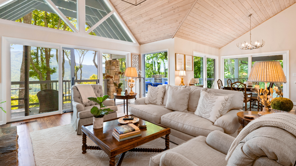 A bright living room with a vaulted wood ceiling, large windows, a cream sectional and a wooden coffee table
