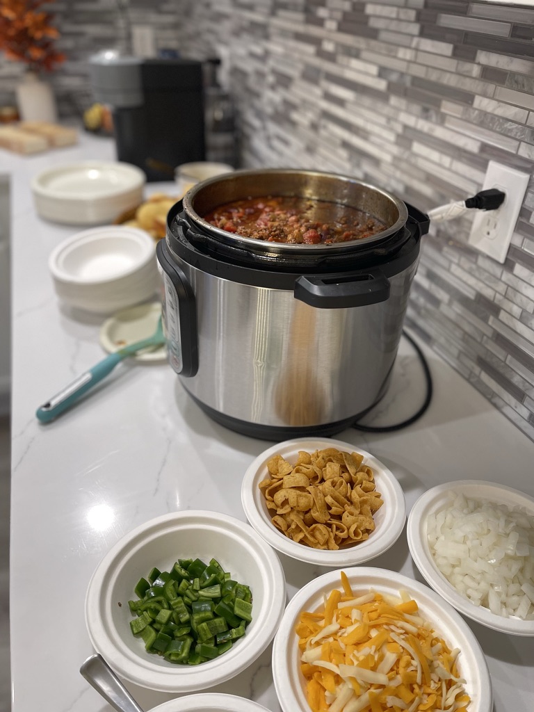 Instant Pot filled with homemade chili beside bowls of Fritos, chopped onions, peppers, and shredded cheese