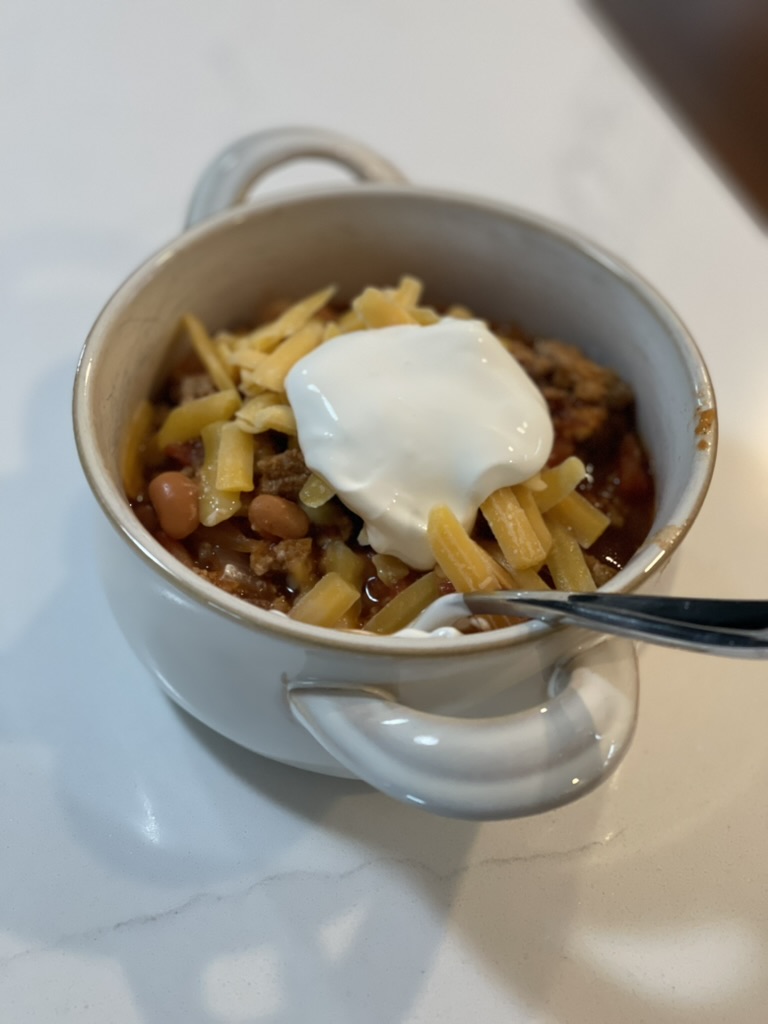 Finished bowl of homemade turkey chili topped with shredded cheddar cheese and sour cream